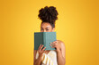 Cheerful young black woman reading book, has fun alone
