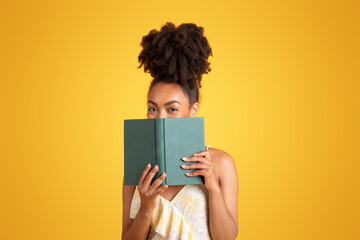 Wall Mural - Cheerful young black woman reading book, has fun alone