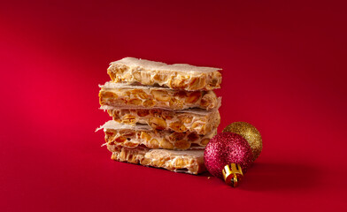 stack of Almond Alicante turron dessert slices with Christmas bolls on red background. traditional dessert in Spain.