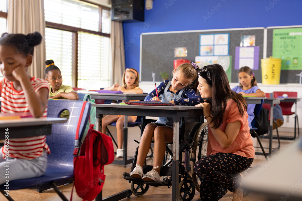Diverse female teacher and schoolgirl in wheelchair in elementary school class
