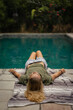 © Cavan Images - A young woman lies by the pool.