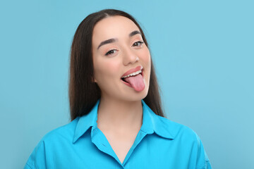 Wall Mural - Happy woman showing her tongue on light blue background