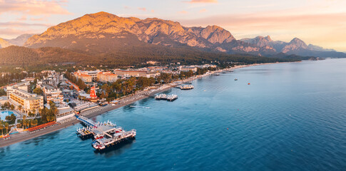Wall Mural - Discover the perfect blend of coastal beauty and mountainous charm with striking aerial photo, showcasing Kemer's hotels overlooking a scenic beach and breathtaking mountains