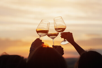 A group of girlfriends raise a toast with glasses of white wine on a sunset. Close shot.	