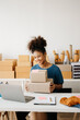 © Nuttapong punna - Young African business owner woman prepare parcel box and standing check online orders for deliver to customer on tablet, laptop Shopping Online concept. in office