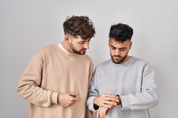 Wall Mural - Young homosexual couple standing over white background checking the time on wrist watch, relaxed and confident