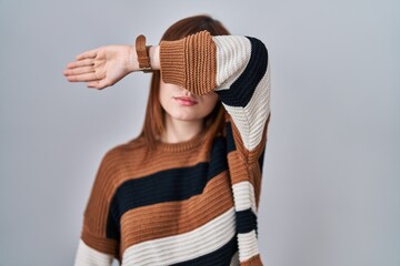 Wall Mural - Young beautiful woman wearing striped sweater over isolated background covering eyes with arm, looking serious and sad. sightless, hiding and rejection concept