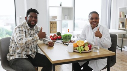 Wall Mural - Portrait of multicultural medical specialist and male patient posing in professional office of modern clinic. Friendly female expert planning nutritional program for active person, thumbs up