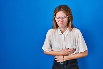 Sticker - Beautiful woman standing over blue background with hand on stomach because nausea, painful disease feeling unwell. ache concept.