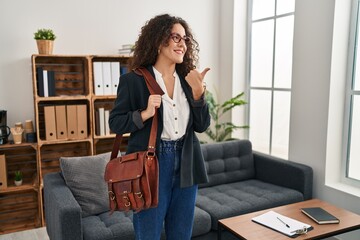 Sticker - Young hispanic woman at consultation office pointing thumb up to the side smiling happy with open mouth