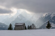 winterliche Landschaft mit Hütte und Bäumen mit besonderem Licht durch die Wolken in den österreichischen Alpen