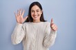 © Krakenimages.com - Young brunette woman standing over blue background showing and pointing up with fingers number six while smiling confident and happy.
