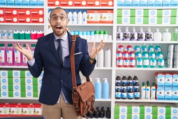 Sticker - Hispanic man with beard working as salesman at pharmacy drugstore celebrating victory with happy smile and winner expression with raised hands