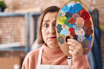 Sticker - Middle age hispanic woman holding painter palette close to face skeptic and nervous, frowning upset because of problem. negative person.