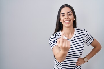 Poster - Young brunette woman wearing striped t shirt beckoning come here gesture with hand inviting welcoming happy and smiling