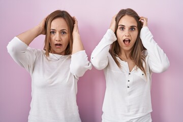 Canvas Print - Middle age mother and young daughter standing over pink background crazy and scared with hands on head, afraid and surprised of shock with open mouth