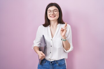 Canvas Print - Young caucasian woman holding laptop gesturing finger crossed smiling with hope and eyes closed. luck and superstitious concept.