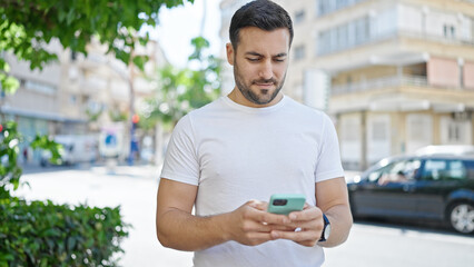 Wall Mural - Young hispanic man using smartphone with serious expression at street