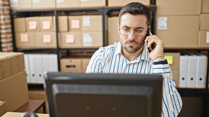 Poster - Young hispanic man ecommerce business worker talking on smartphone using computer at office