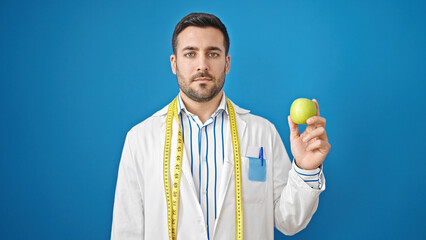 Poster - Young hispanic man dietician holding apple over isolated blue background