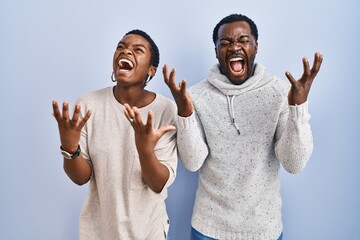 Poster - Young african american couple standing over blue background together celebrating mad and crazy for success with arms raised and closed eyes screaming excited. winner concept