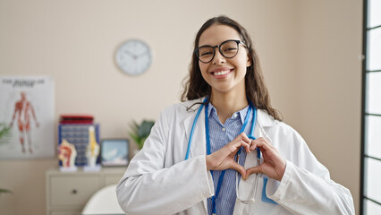 Poster - Young beautiful hispanic woman doctor smiling doing heart gesture with hands at clinic