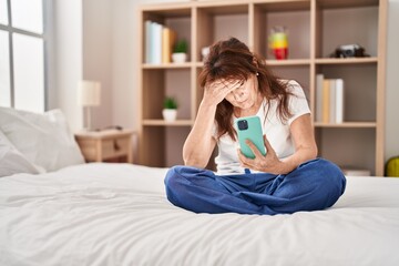 Wall Mural - Middle age woman using smartphone wit worried expression at bedroom