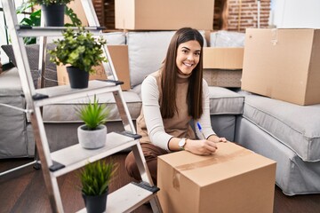 Sticker - Young beautiful hispanic woman smiling confident writing on package at new home