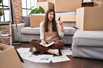 Poster - Young brunette woman moving to a new home doing finances surprised with an idea or question pointing finger with happy face, number one