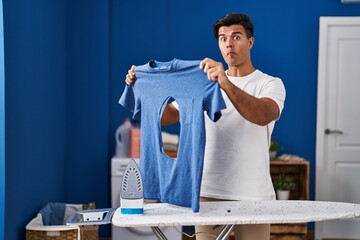 Poster - Hispanic man ironing holding burned iron shirt at laundry room making fish face with mouth and squinting eyes, crazy and comical.