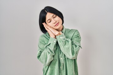 Poster - Young asian woman standing over white background sleeping tired dreaming and posing with hands together while smiling with closed eyes.