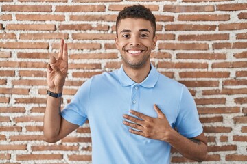 Sticker - Brazilian young man standing over brick wall smiling swearing with hand on chest and fingers up, making a loyalty promise oath