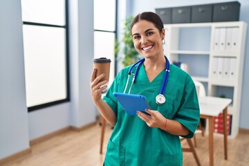 Sticker - Young beautiful hispanic woman doctor using touchpad drinking coffee at clinic