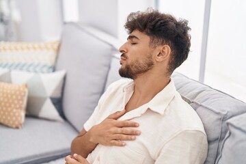 Sticker - Young arab man suffering heart attack sitting on sofa at home