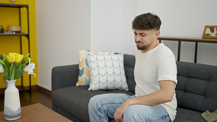 Wall Mural - Young arab man suffering for backache sitting on sofa at home