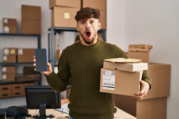 Wall Mural - Arab man with beard working at small business ecommerce holding delivery packages afraid and shocked with surprise and amazed expression, fear and excited face.