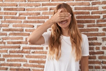 Sticker - Young caucasian woman standing over bricks wall smiling and laughing with hand on face covering eyes for surprise. blind concept.