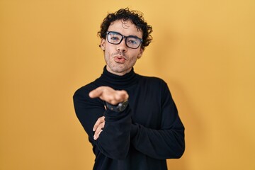 Wall Mural - Hispanic man standing over yellow background looking at the camera blowing a kiss with hand on air being lovely and sexy. love expression.