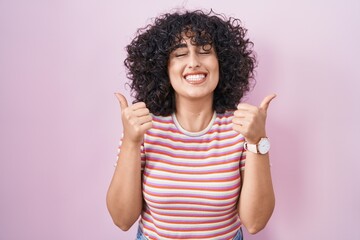 Sticker - Young middle east woman standing over pink background success sign doing positive gesture with hand, thumbs up smiling and happy. cheerful expression and winner gesture.