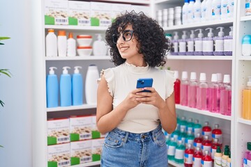 Poster - Young middle eastern woman customer smiling confident using smartphone at pharmacy