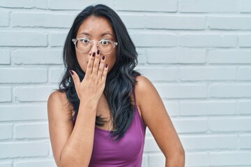 Canvas Print - Asian young woman standing over bricks background covering mouth with hand, shocked and afraid for mistake. surprised expression