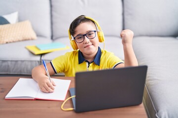 Sticker - Young hispanic kid doing homework with laptop at home screaming proud, celebrating victory and success very excited with raised arm