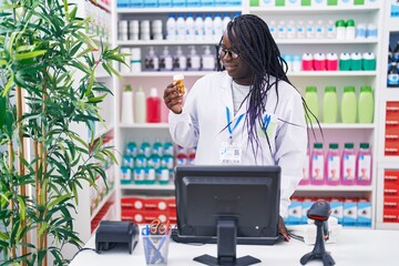 Canvas Print - African american woman pharmacist using computer holding pills bottle at pharmacy