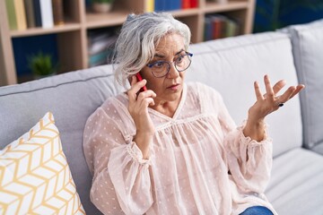 Poster - Middle age grey-haired woman talking on smartphone with worried expression at home