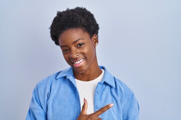 Wall Mural - African american woman standing over blue background cheerful with a smile on face pointing with hand and finger up to the side with happy and natural expression