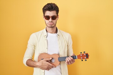 Canvas Print - Young hispanic man playing ukulele over yellow background depressed and worry for distress, crying angry and afraid. sad expression.