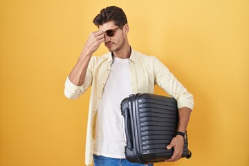 Wall Mural - Young hispanic man holding suitcase going on summer vacation tired rubbing nose and eyes feeling fatigue and headache. stress and frustration concept.