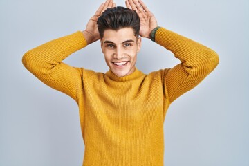 Wall Mural - Young hispanic man standing over blue background doing bunny ears gesture with hands palms looking cynical and skeptical. easter rabbit concept.