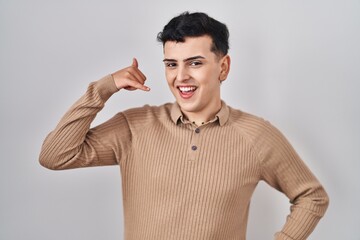 Canvas Print - Non binary person standing over isolated background smiling doing phone gesture with hand and fingers like talking on the telephone. communicating concepts.