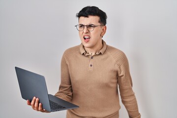 Wall Mural - Non binary person using computer laptop angry and mad screaming frustrated and furious, shouting with anger. rage and aggressive concept.